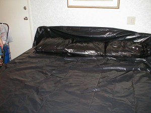 Hotel room bed covered in black plastic, complete with pillows in black trash bags